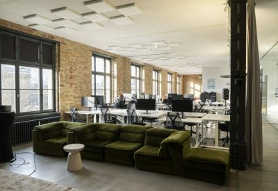Spacious open-plan workspace with large industrial windows and a long green velvet sectional sofa.