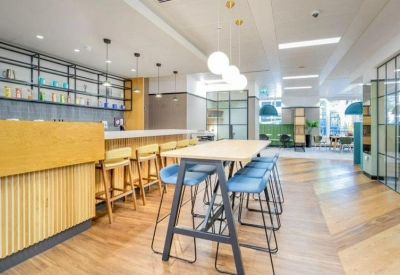 Bright coworking kitchen and lounge with light wood cabinetry and blue bar stools.