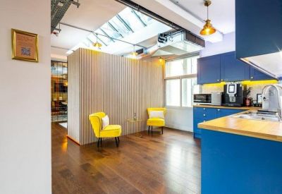 Bright communal kitchen with blue cabinets, yellow armchairs, and a large skylight.