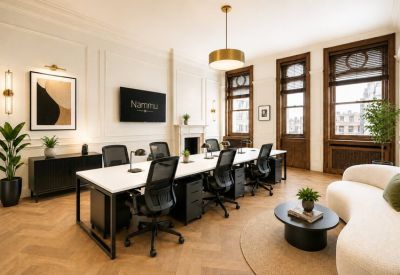 Spacious open-plan workspace with sleek white desks, ergonomic black chairs, and large historic windows.