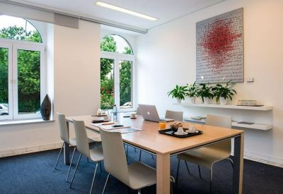 Bright meeting room with a wooden table, red abstract art, and potted plants.