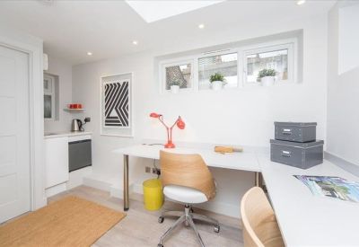 Modern office nook with wooden desk chairs and a small kitchen area in the background.