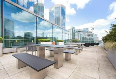 Sunny outdoor roof terrace featuring stone picnic tables and glass railings.