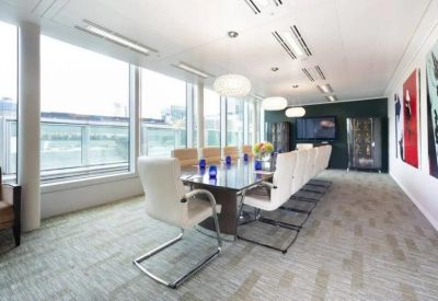 Bright boardroom with a long glass table, white ergonomic chairs, and large windows.