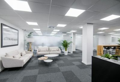 Modern lounge area with grey sofas, white coffee tables, and indoor plants.