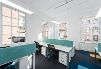 Bright open-plan office space with white desks, teal partitions, and large windows.