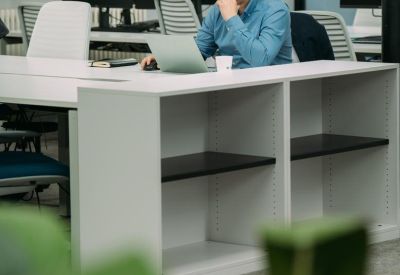 Person working at a white desk with integrated shelving in a shared office space.