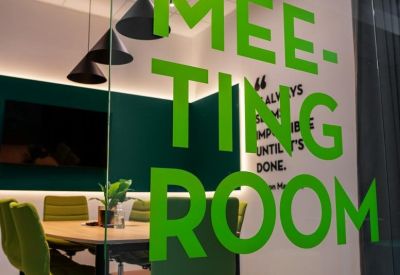 Glass-walled meeting room with green chairs and black pendant lights.