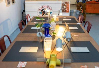 Long wooden coworking table with individual desk lamps and black placemats near a branded bar.