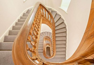 Ornate spiral staircase with a polished wood banister and grey carpet.
