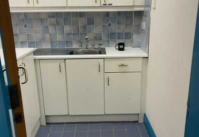 Compact kitchenette with white cabinetry and blue tiled backsplash.