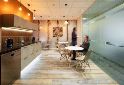 Modern communal kitchen and breakout area with warm orange walls and wooden flooring.