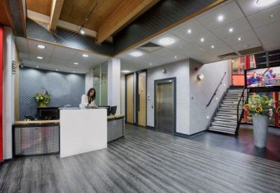 Bright reception area featuring a white desk, grey wood-effect flooring, and a modern staircase.