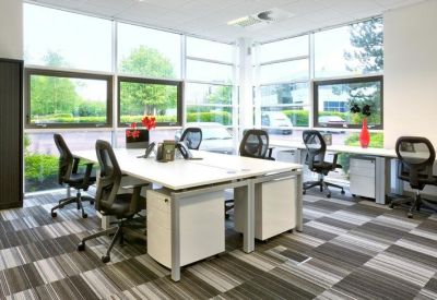 Open-plan office space with white desks, ergonomic black chairs, and large windows overlooking greenery.