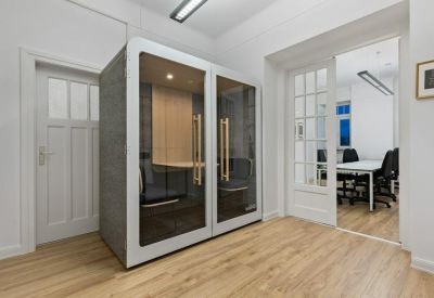 Private glass-walled phone booths in a bright room with wooden flooring.