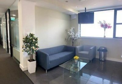 Bright communal lounge with a blue sofa, glass coffee table, and indoor plants.