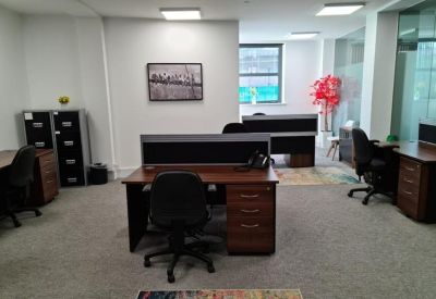 Open-plan office space with several dark wood desks and black ergonomic chairs.