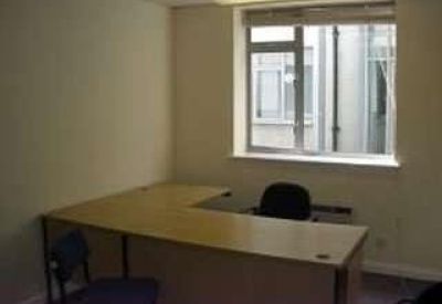 Simple private office with an L-shaped wooden desk and a window overlooking a courtyard.