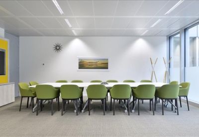 Spacious boardroom with a large white table and green modern chairs under bright recessed lighting.