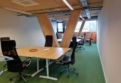 Bright office space with wooden desks, ergonomic chairs, and green carpeting.