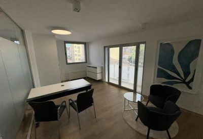 Bright private office with a dark desk, armchairs, and a large abstract blue painting.