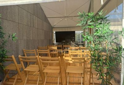 Outdoor meeting space under a white canopy with rows of wooden folding chairs.