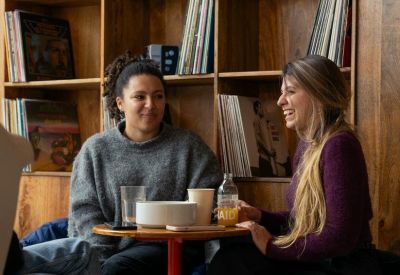Cozy common area with two women chatting near a wooden shelf filled with vinyl records.