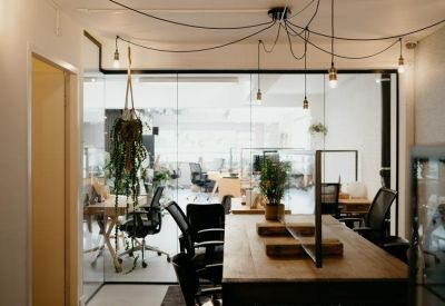 Bright open-plan workspace with wooden desks, ergonomic chairs, and glass partitions.