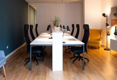 Long white communal desk with black ergonomic chairs and a yellow wingback armchair.