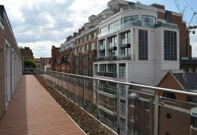 Long rooftop terrace with wooden decking and glass railings overlooking neighboring city buildings.