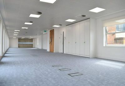 Bright, empty open-plan office space with grey carpeting and large windows.