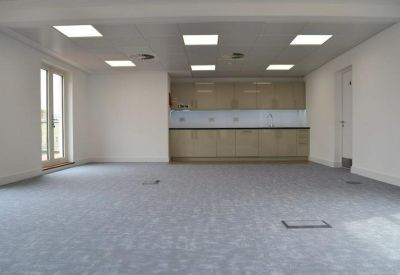 Sleek office kitchenette with light wood cabinetry and a white tiled backsplash.