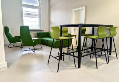 High-top meeting table with vibrant green stools near a window and lounge seating.