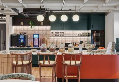 Modern office kitchen featuring a colorful red island and dark green cabinetry.