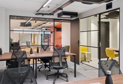 Open-plan office space with wooden desks and black ergonomic mesh chairs.