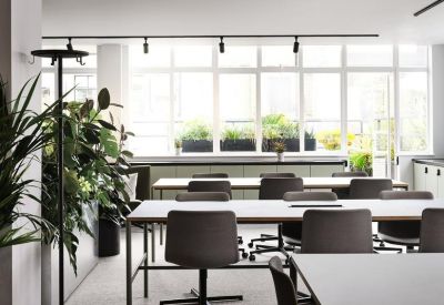 Open-plan office with multiple rows of desks and large windows providing natural light.