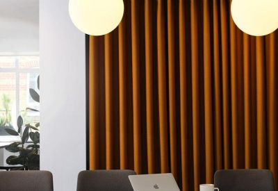 Close-up of a conference table with grey chairs, a laptop, and a vibrant orange backdrop.