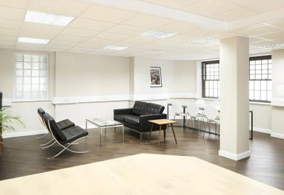 Spacious breakout lounge featuring black leather sofas, designer chairs, and parquet flooring.