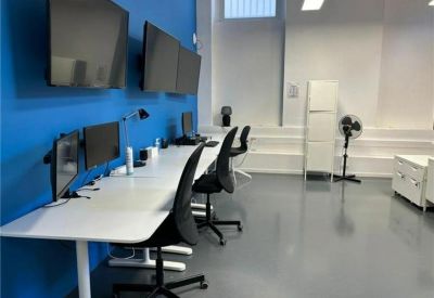 Modern open-plan workspace with white desks and dual monitors against a bright blue wall.
