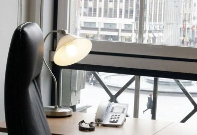 Close-up of a desk with a lamp and telephone beside a large window.