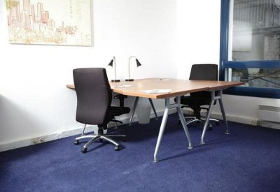 Bright workspace featuring two dark chairs and a wooden desk on blue carpeting.