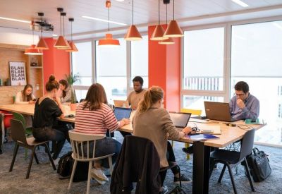 Vibrant coworking space with orange pillars, hanging pendant lights, and people working at a shared table.