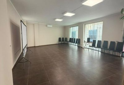 Wide meeting room with a rows of black chairs, a projector screen, and large windows.