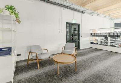 Lounge area with two grey armchairs and a round wooden coffee table on a grey carpet.