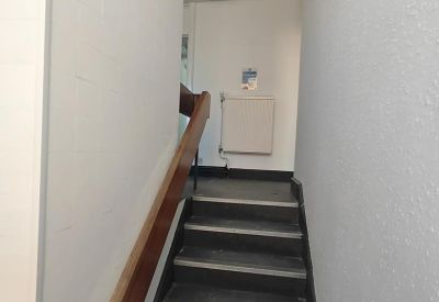 Narrow concrete staircase with a wooden handrail leading to an upper floor.