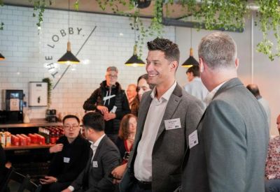 Lively coworking lounge with people networking near a coffee bar and hanging greenery.