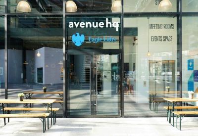 Modern glass entrance with branded signage and outdoor picnic tables.