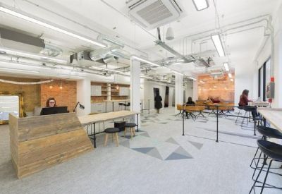 Spacious open-plan coworking area with a wooden reception desk and industrial ceiling.