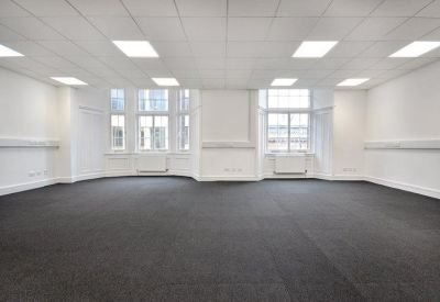 Bright, empty open-plan office space with grey carpet and multiple windows.