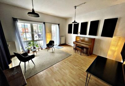 Bright multi-purpose room featuring soundproofing panels, a piano, and lounge seating.